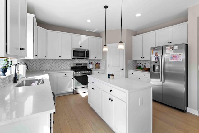 kitchen featuring light wood-type flooring, stainless steel appliances, sink, decorative light fixtures, and a kitchen island