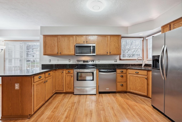 kitchen featuring kitchen peninsula, stainless steel appliances, sink, light hardwood / wood-style flooring, and dark stone countertops