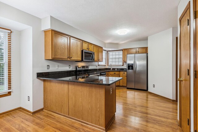 kitchen with dark stone counters, sink, light hardwood / wood-style floors, kitchen peninsula, and stainless steel appliances