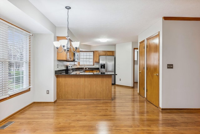 kitchen with decorative light fixtures, light wood-type flooring, a notable chandelier, kitchen peninsula, and stainless steel appliances