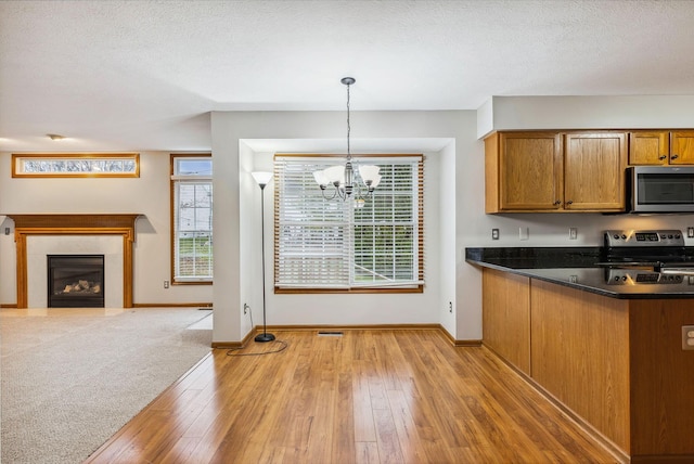 kitchen featuring light hardwood / wood-style floors, a textured ceiling, a chandelier, decorative light fixtures, and appliances with stainless steel finishes