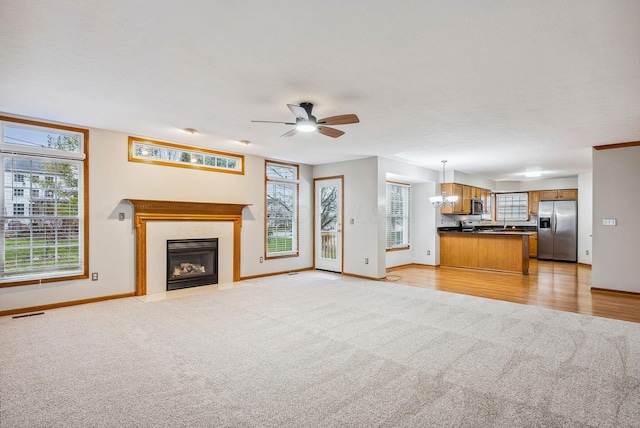 unfurnished living room with light carpet and ceiling fan with notable chandelier