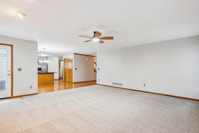 unfurnished living room with light carpet and ceiling fan with notable chandelier