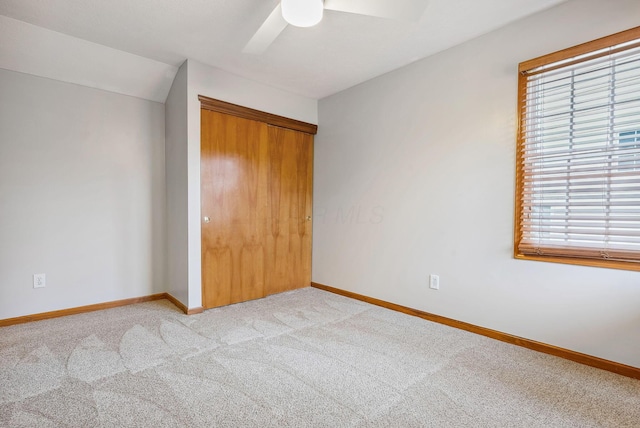 unfurnished bedroom featuring ceiling fan, a closet, light colored carpet, and lofted ceiling