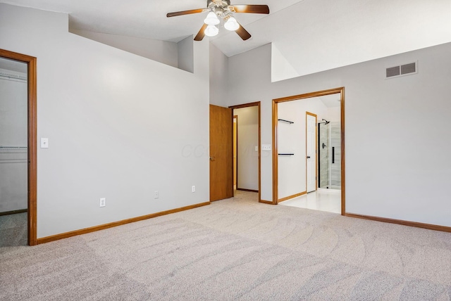 unfurnished bedroom with ensuite bath, ceiling fan, high vaulted ceiling, and light colored carpet