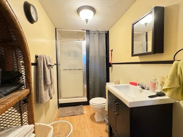 bathroom with walk in shower, wood-type flooring, a textured ceiling, toilet, and vanity