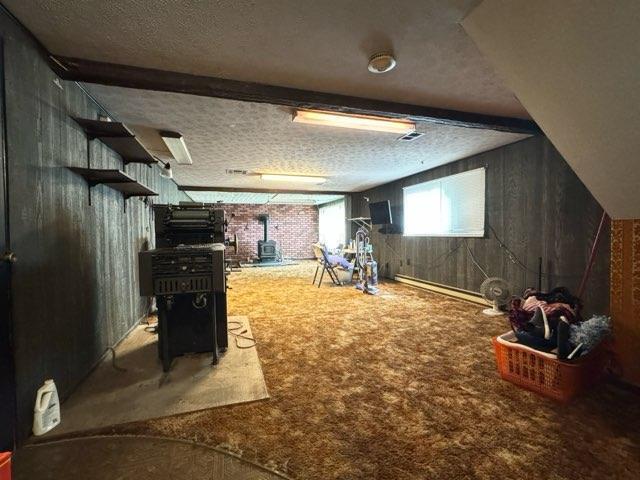 interior space featuring beam ceiling, a wood stove, wood walls, carpet floors, and a textured ceiling