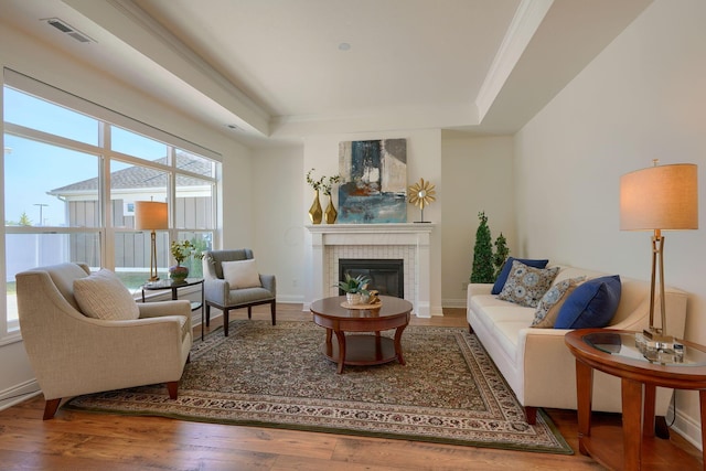 living room featuring a tray ceiling, a fireplace, crown molding, and hardwood / wood-style floors