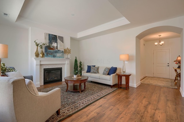 living room featuring wood-type flooring, a tray ceiling, a notable chandelier, and a tiled fireplace