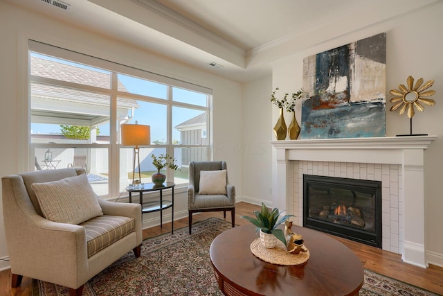 sitting room featuring a tray ceiling, a tiled fireplace, wood-type flooring, and ornamental molding