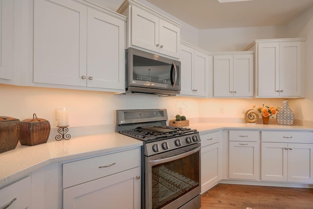 kitchen with stainless steel appliances, white cabinetry, and light hardwood / wood-style flooring