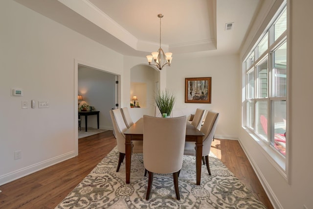 dining space featuring a raised ceiling, crown molding, a chandelier, and dark hardwood / wood-style floors