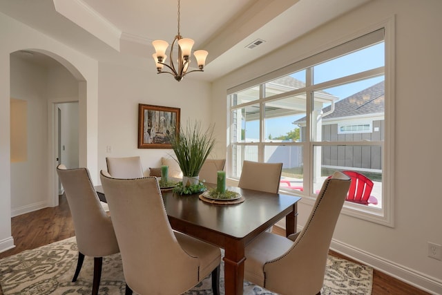 dining area with a tray ceiling, dark wood-type flooring, and a notable chandelier