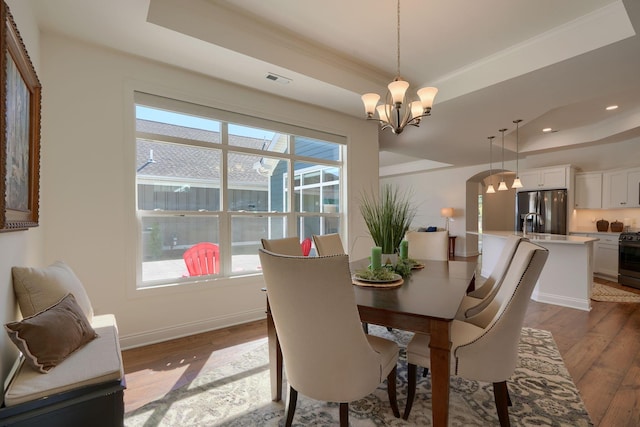 dining room with a chandelier, hardwood / wood-style floors, a tray ceiling, and ornamental molding