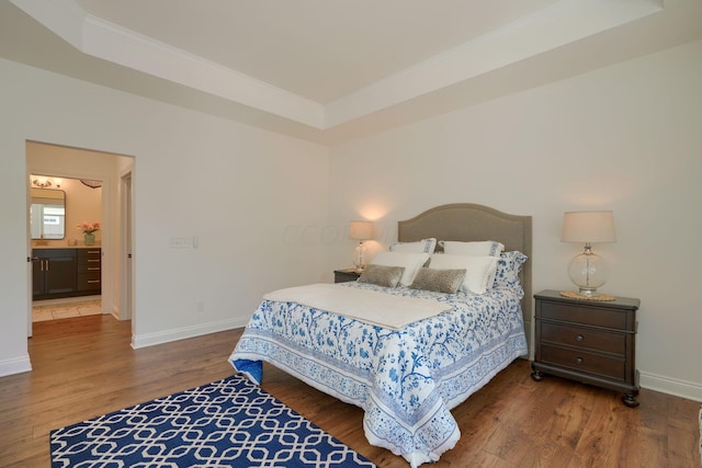 bedroom with a tray ceiling, connected bathroom, and wood-type flooring