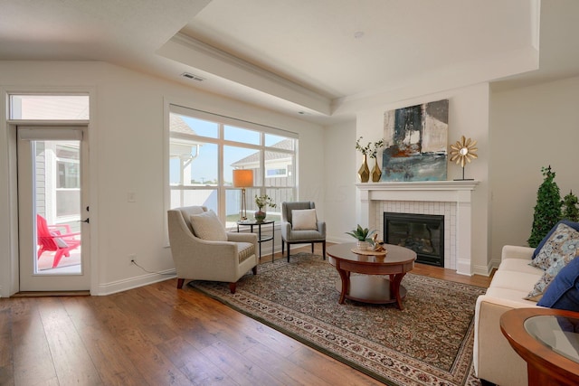 interior space with a tray ceiling, a tile fireplace, and hardwood / wood-style flooring