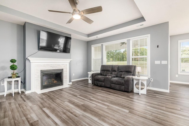 living room with ceiling fan, light wood-type flooring, a fireplace, and a tray ceiling