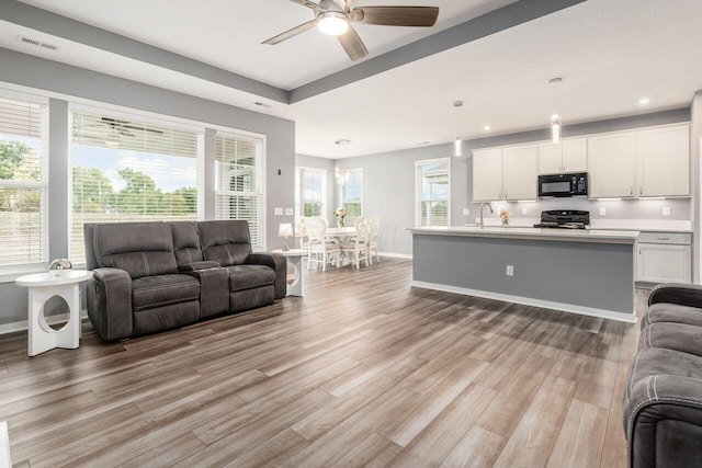 living room with plenty of natural light, light hardwood / wood-style floors, sink, and ceiling fan