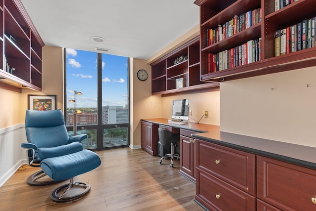 office space featuring expansive windows, built in desk, and light hardwood / wood-style floors