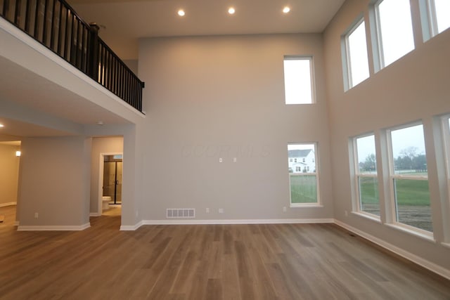 unfurnished living room featuring a high ceiling, hardwood / wood-style floors, and a wealth of natural light