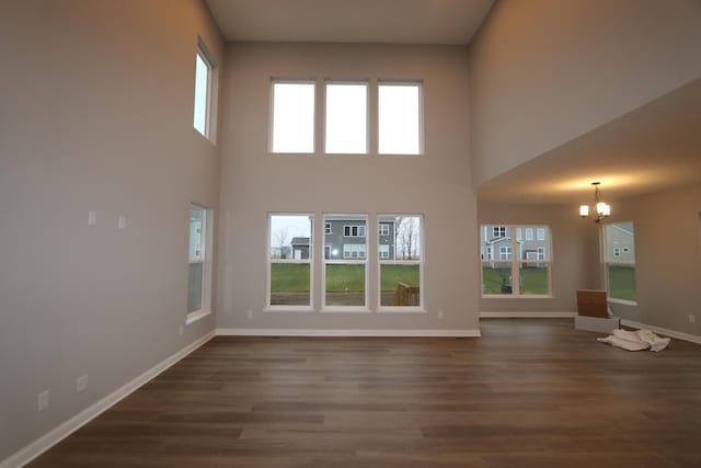 unfurnished living room featuring a notable chandelier, dark wood-type flooring, and a high ceiling