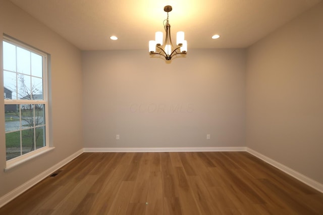 spare room with a chandelier, a healthy amount of sunlight, and dark hardwood / wood-style floors