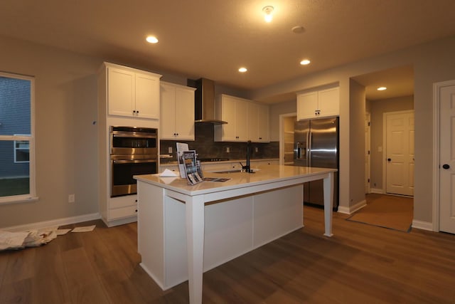 kitchen featuring white cabinets, wall chimney exhaust hood, an island with sink, dark hardwood / wood-style flooring, and appliances with stainless steel finishes