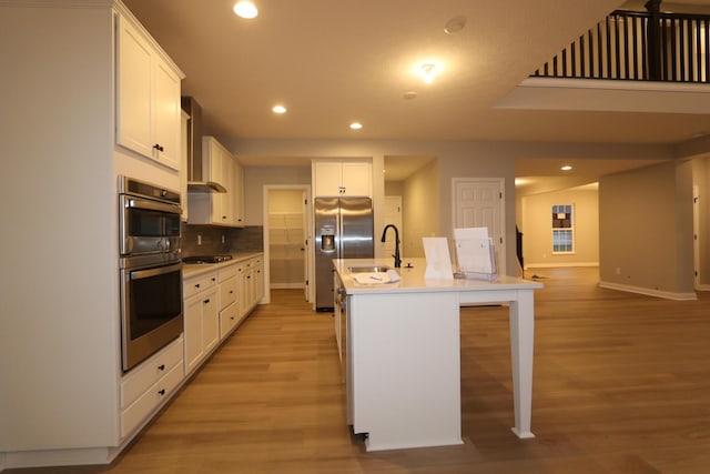 kitchen featuring a kitchen breakfast bar, a center island with sink, appliances with stainless steel finishes, sink, and white cabinetry