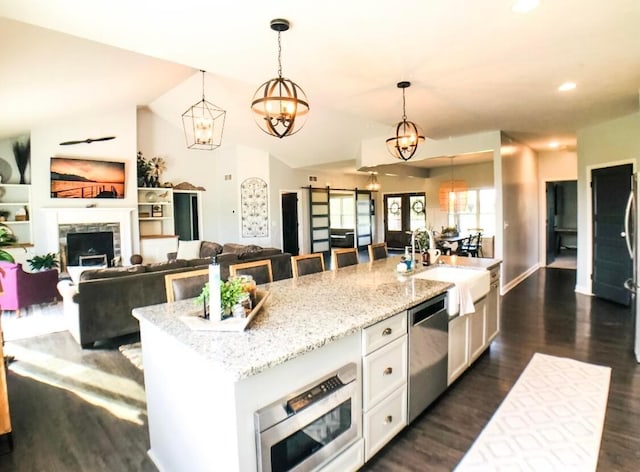 kitchen featuring a center island with sink, dishwasher, light stone counters, and hanging light fixtures