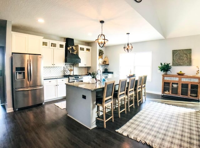 kitchen with appliances with stainless steel finishes, premium range hood, pendant lighting, white cabinetry, and an island with sink