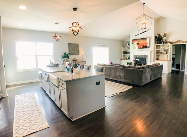 kitchen with a fireplace, light stone counters, a center island with sink, and decorative light fixtures