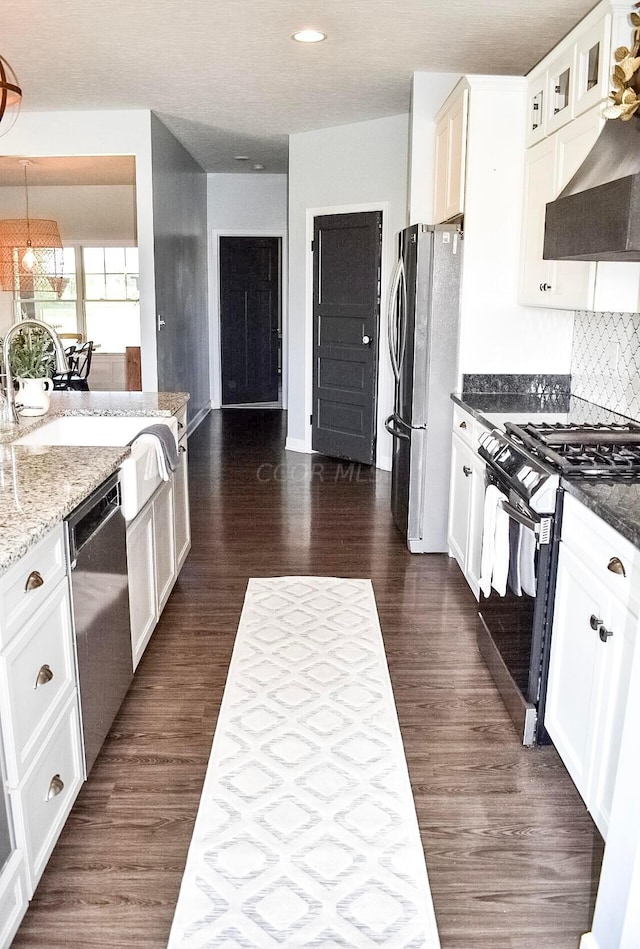 kitchen featuring appliances with stainless steel finishes, tasteful backsplash, dark stone counters, white cabinets, and hanging light fixtures