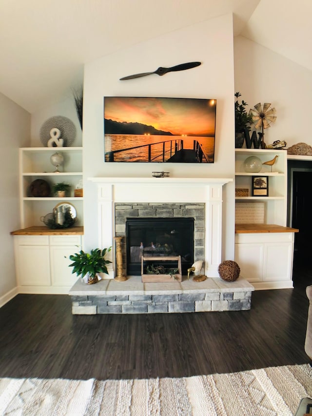 unfurnished living room with vaulted ceiling, a stone fireplace, and dark wood-type flooring