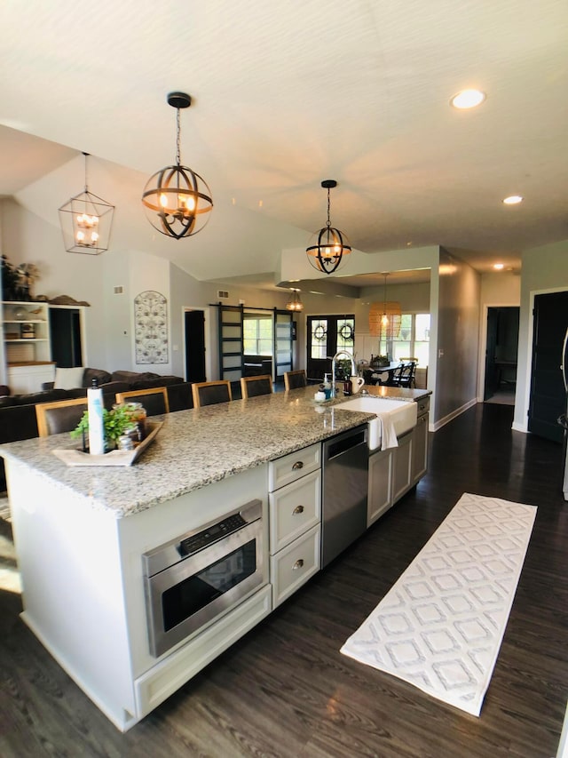 kitchen with stainless steel dishwasher, pendant lighting, a center island with sink, and light stone counters