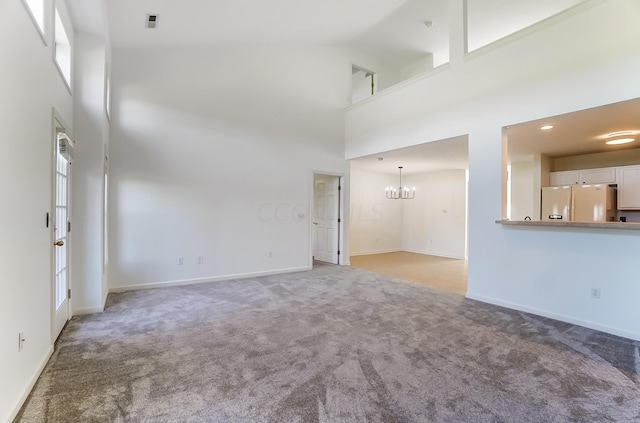 unfurnished living room with light carpet, a notable chandelier, and a high ceiling