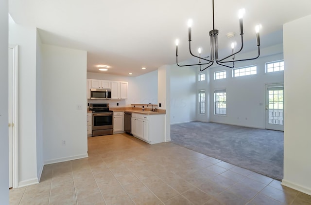 kitchen featuring pendant lighting, white cabinets, appliances with stainless steel finishes, an inviting chandelier, and light colored carpet