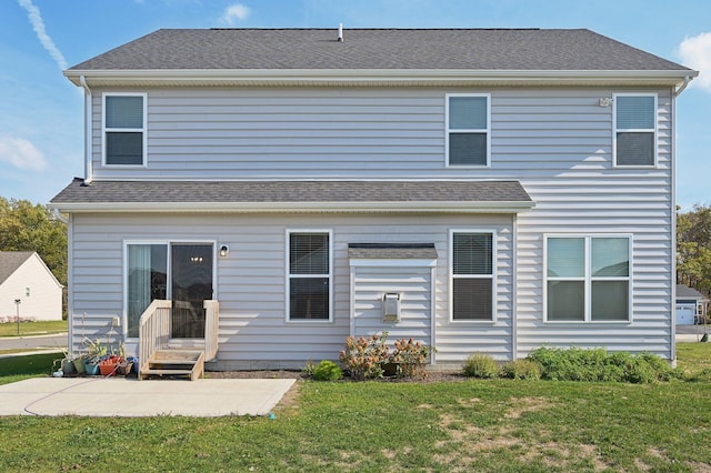 rear view of house featuring entry steps, a patio area, roof with shingles, and a lawn