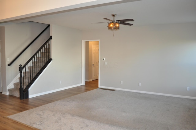 empty room featuring a ceiling fan, stairway, baseboards, and wood finished floors