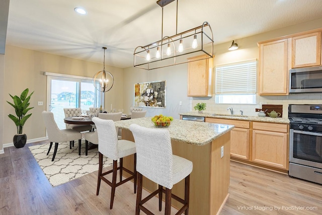 kitchen with a breakfast bar, backsplash, appliances with stainless steel finishes, light brown cabinets, and a sink