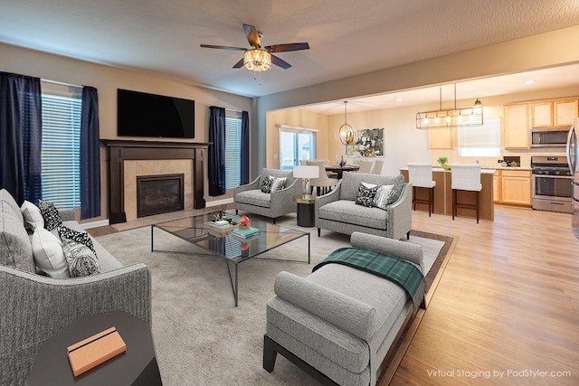 living area with light wood-style floors, ceiling fan with notable chandelier, and a tile fireplace