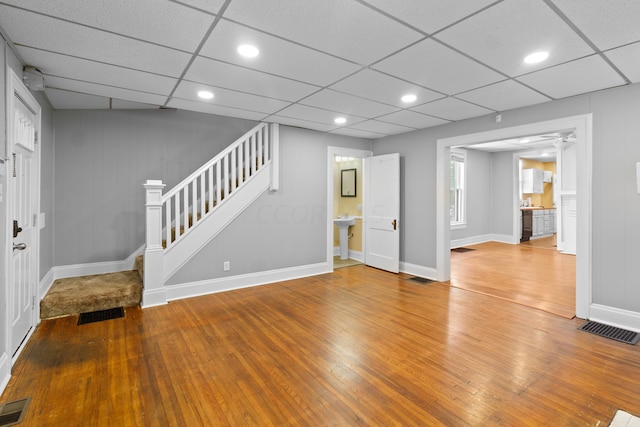 interior space with wooden walls, a drop ceiling, and hardwood / wood-style flooring