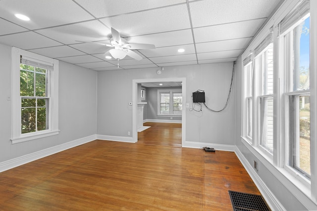 empty room featuring ceiling fan, plenty of natural light, wood-type flooring, and a drop ceiling