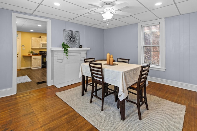 dining area with ceiling fan, baseboards, a drop ceiling, and dark wood-type flooring