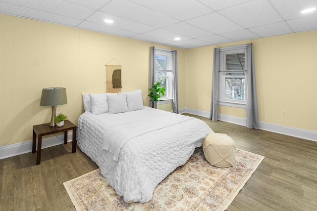 bedroom with recessed lighting, a drop ceiling, baseboards, and wood finished floors