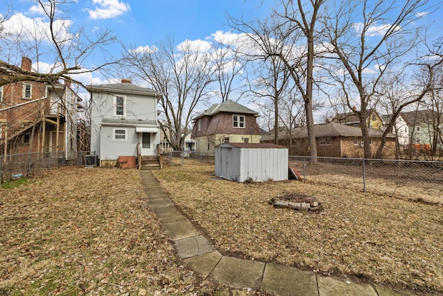 view of yard with entry steps, a fenced backyard, an outbuilding, a storage unit, and central air condition unit