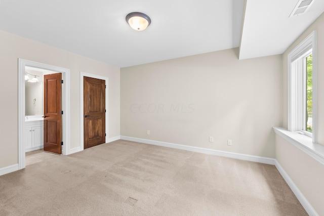 unfurnished bedroom with light carpet, connected bathroom, and multiple windows