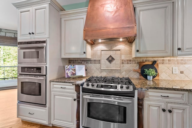 kitchen with decorative backsplash, light hardwood / wood-style floors, custom range hood, and appliances with stainless steel finishes