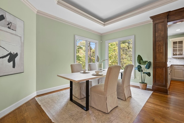 dining room with light wood-type flooring, ornamental molding, a tray ceiling, and decorative columns