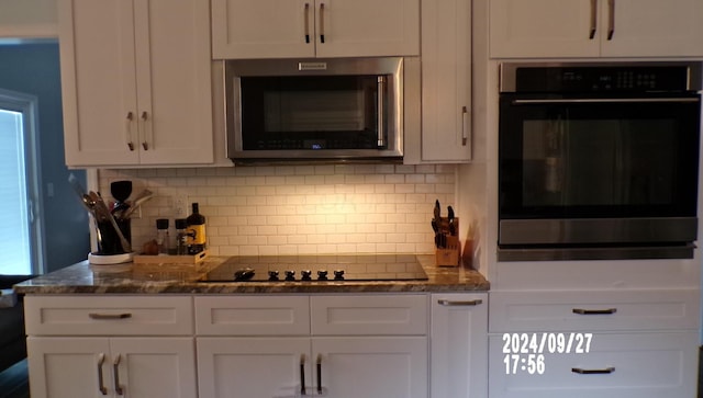 kitchen featuring white cabinets, backsplash, stainless steel appliances, and dark stone counters