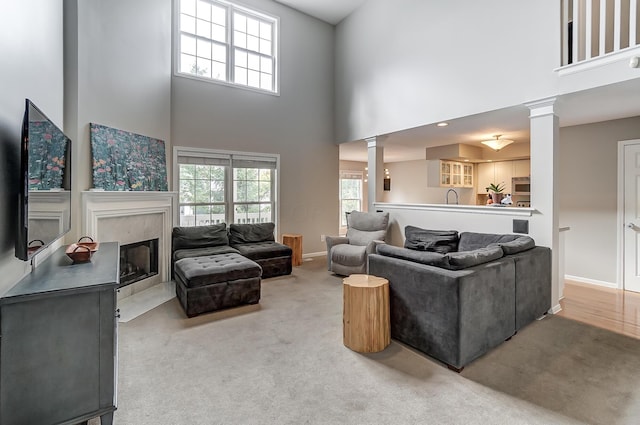 living room featuring carpet flooring, sink, decorative columns, a towering ceiling, and a fireplace